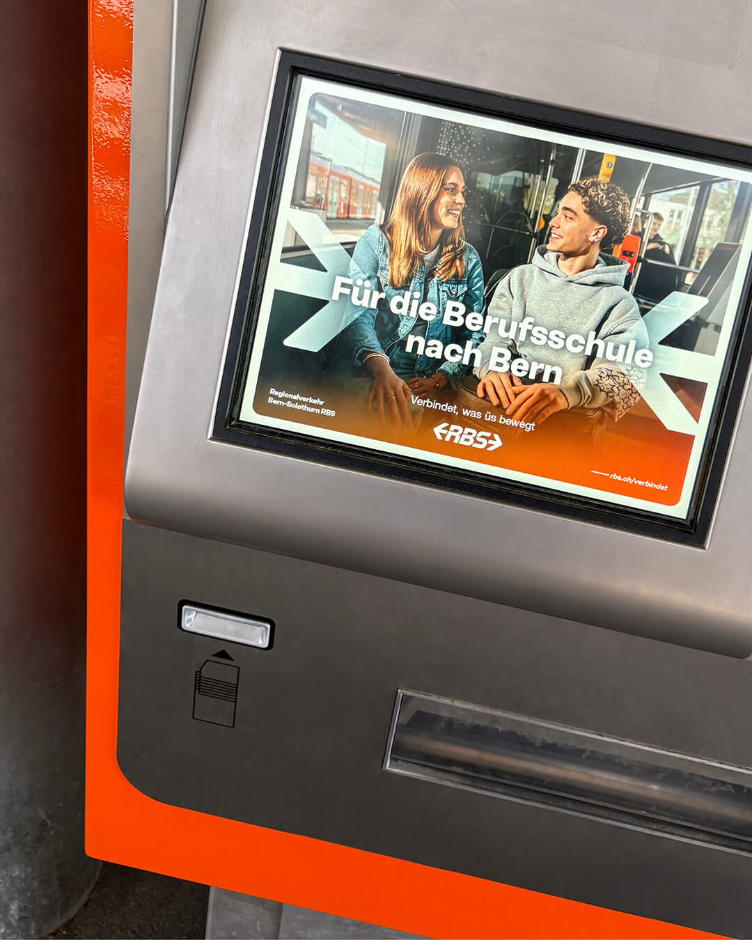Ticketautomat-Mockup mit RBS-Kampagnensujet. Zu sehen sind zwei Jugendliche in einer Bahn und der Text «Für die Berufsschule nach Bern».