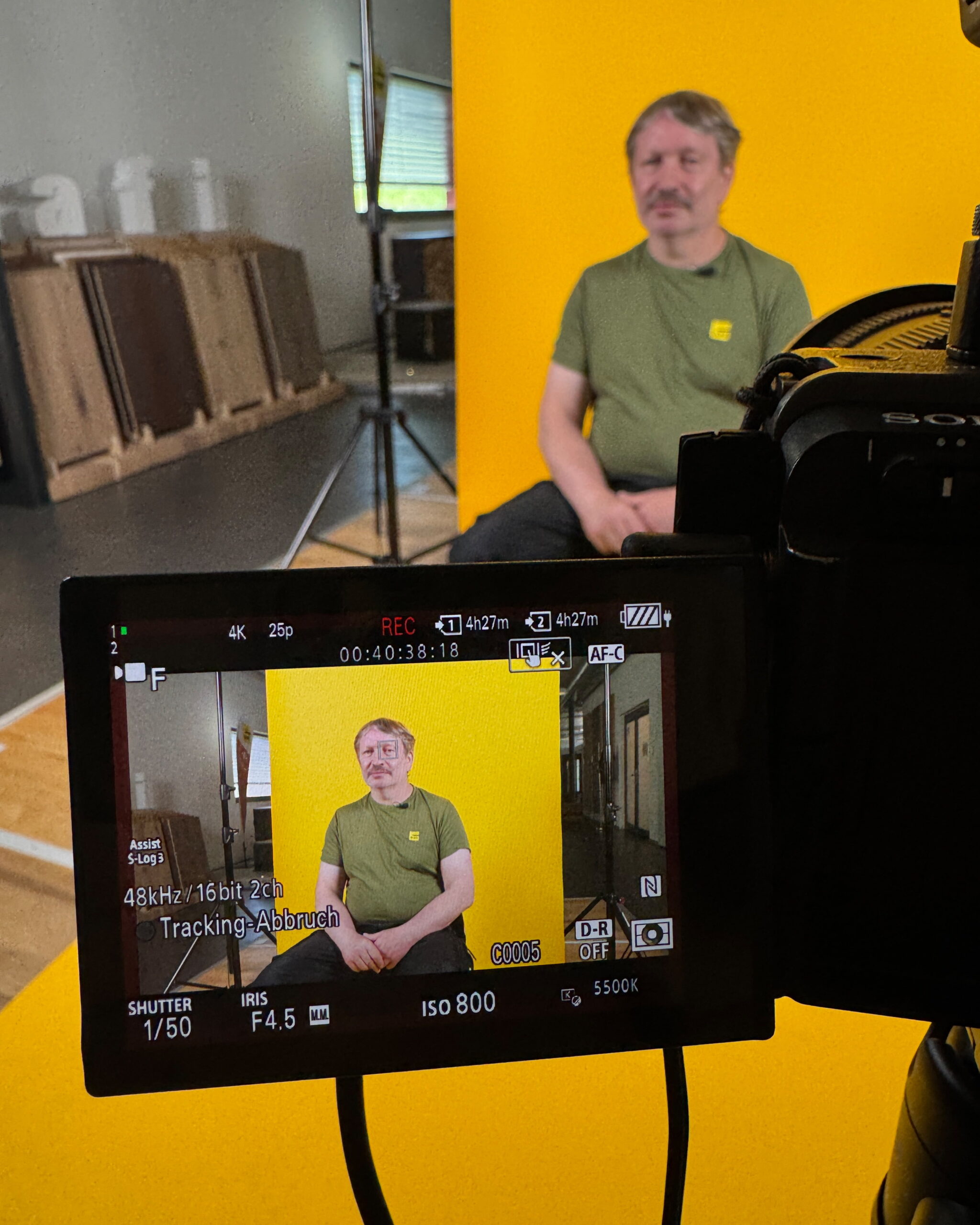 Behind the Scenes beim Jubiläumsdreh für OLWO: Ein Mitarbeiter sitzt vor gelbem Hintergrund vor der Kamera.